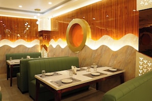 A restaurant interior with green upholstered booths, a marble-topped dining table, and a decorative wall with a circular design.