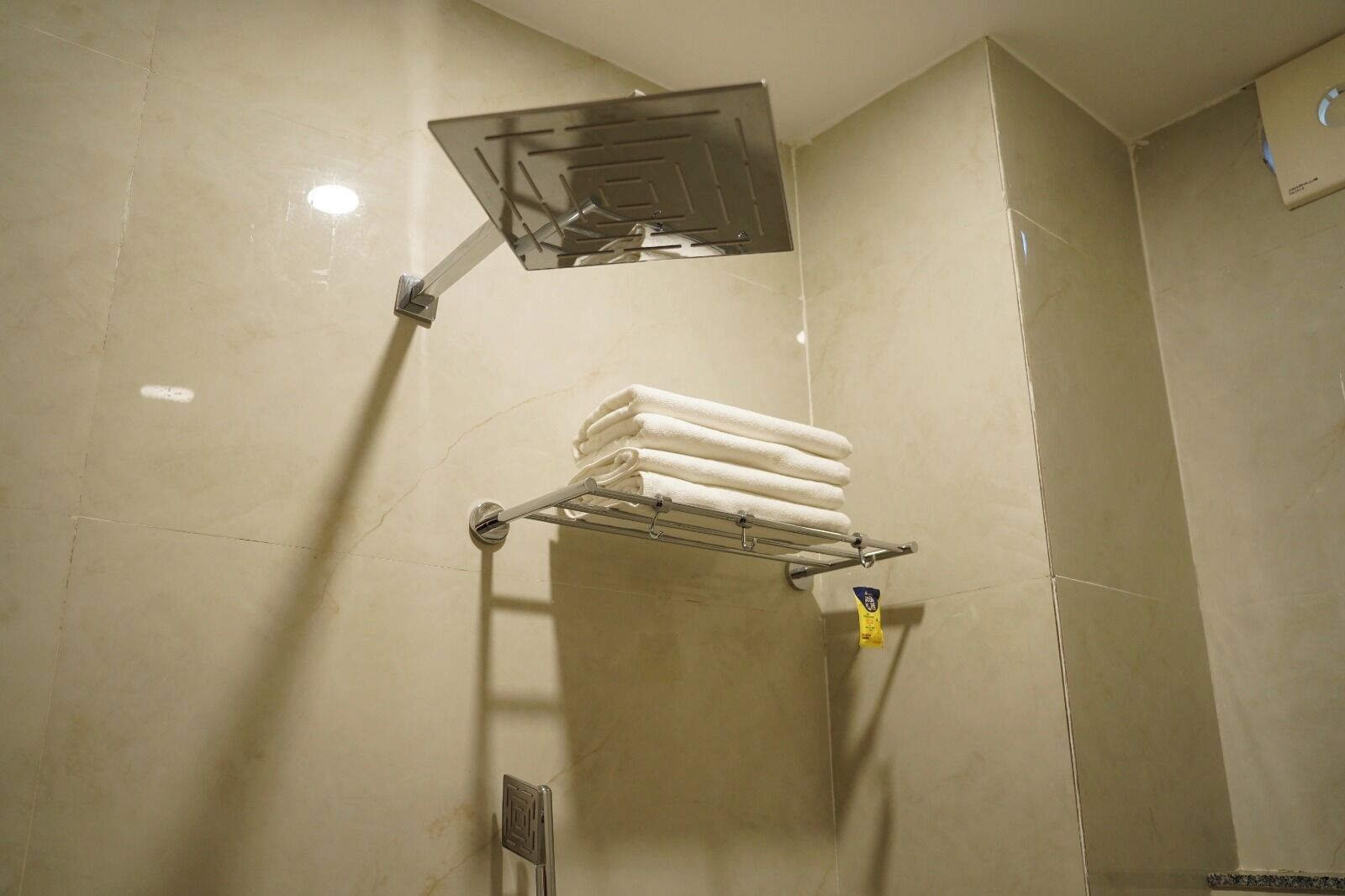 Casa de banho com chuveiro, toalheiro com toalhas dobradas e dispensador de sabonete.