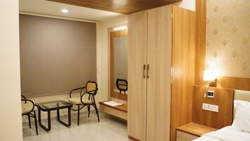 A hotel room with a bed, a desk with a chair, a wardrobe, and a bedside table with a lamp.