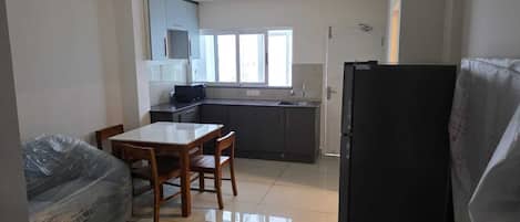 A compact kitchen with a dining table, chairs, a refrigerator, and a window.