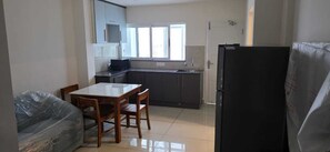 A compact kitchen with a dining table, chairs, a refrigerator, and a window. - Lovely 2-bedroom apartment with AC for a relaxing stay (Ernakulam)