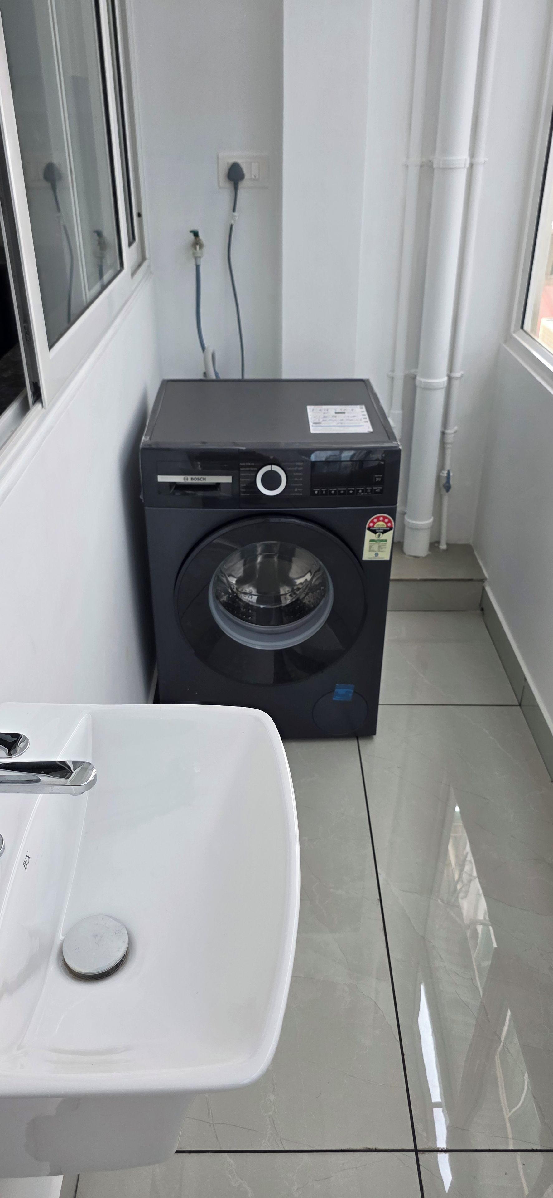 A compact laundry area with a Bosch washing machine, a white sink, and tiled flooring.
