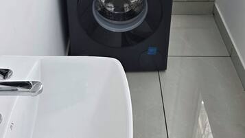 A compact laundry area with a Bosch washing machine, a white sink, and tiled flooring.
