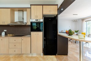 Una cuina moderna amb armaris de fusta, una campana extractora d'acer inoxidable, un frigorífic negre i una zona de dinar amb taula i cadires.