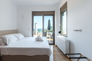 A hotel room with a bed, a view of the sea, and a balcony with a table and chairs. - Seaside House (Galatas)