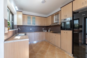 Eine moderne Küche mit Holzschränken, einer Edelstahl-Spüle und einem schwarzen Kühlschrank.