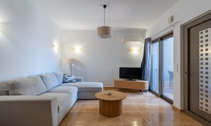A modern living room with a sofa, a coffee table, a TV, and a sliding glass door. - Seaside House (Galatas)