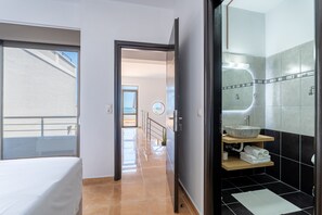 A hotel room with a bed, a bathroom with a stone sink, and a view of the sea through the window. - Seaside House (Galatas)