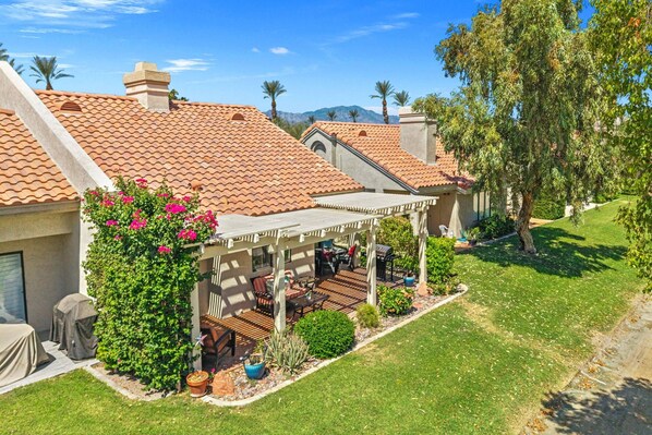 A residential property with a covered patio, a lawn, and a mountain backdrop.