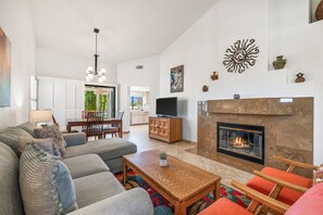 A spacious living room with a fireplace, a dining area, and a kitchen visible through an open door.