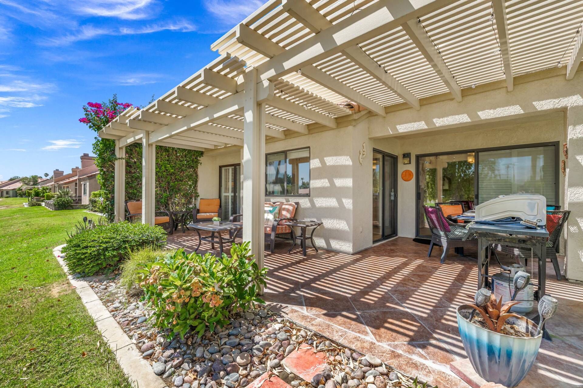 Eine überdachte Terrasse mit Gartenmöbeln, einem Grill und einem Garten mit verschiedenen Pflanzen.