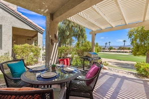 An outdoor patio with a round glass table set for dining, surrounded by wicker chairs with cushions. - Palm Desert Resort Condo | Preston Trail | Near Indian Wells Tennis Garden & Golf (Palm Desert)