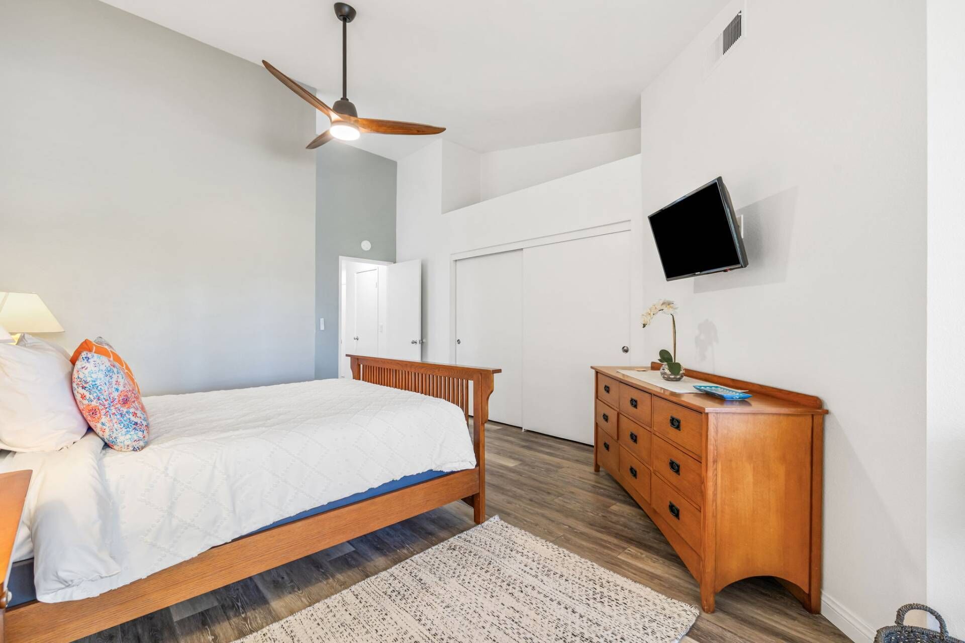 Una camera da letto con un letto, una cassettiera in legno, una televisione montata a parete e una ventola a soffitto.