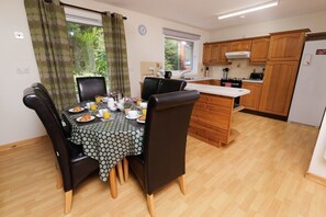 A dining area with a table set for breakfast, a kitchen with wooden cabinets, and a view of greenery outside.