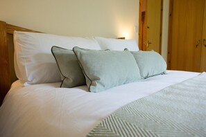 A bed with white bedding and two pillows, a wooden headboard, and a door in the background.