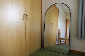 Een kamer met een houten garderobe, een spiegel die een stoel en een deur weerspiegelt, en een vloerbedekking.