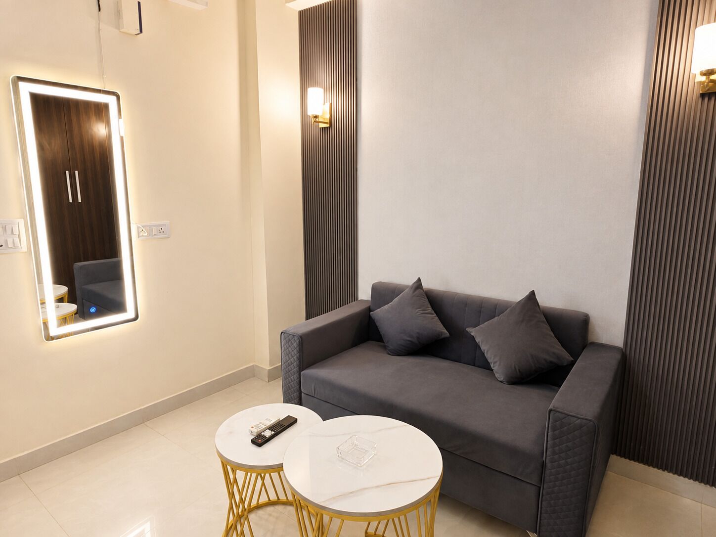 Una sala de estar moderna con un sofá gris, dos mesitas redondas y un espejo colgado en la pared.
