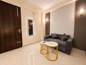 Uma sala de estar moderna com um sofá cinzento, duas mesas redondas pequenas com pés amarelos e um espelho grande com iluminação embutida.