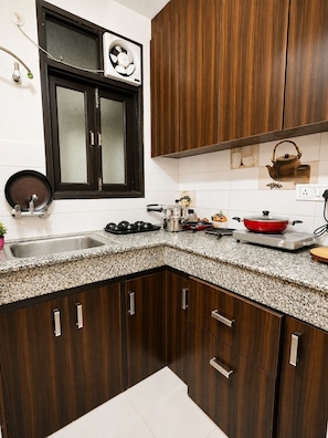 Cozinha com armários de madeira escura, bancada de granito, janela com ventilador e diversos eletrodomésticos.