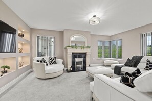 Ein modernes Wohnzimmer mit Kamin, weißen Sofas und einem großen Fenster mit Jalousien.