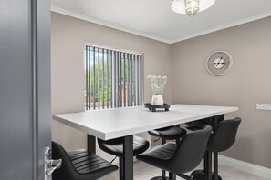 A dining area with a white table, black chairs, a potted plant, a clock, and a window with vertical blinds. - Hot tub, golf views, sleeps 10 — 400m from Lough Erne (Enniskillen)