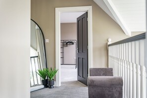 Ein Flur mit einer Tür zu einem Zimmer, einem Blumentopf, einem grauen Stuhl und einem weißen Geländer.