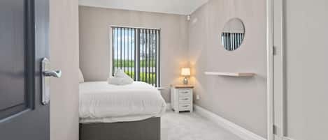 A bedroom with a bed, bedside table, lamp, and a view through the window.
