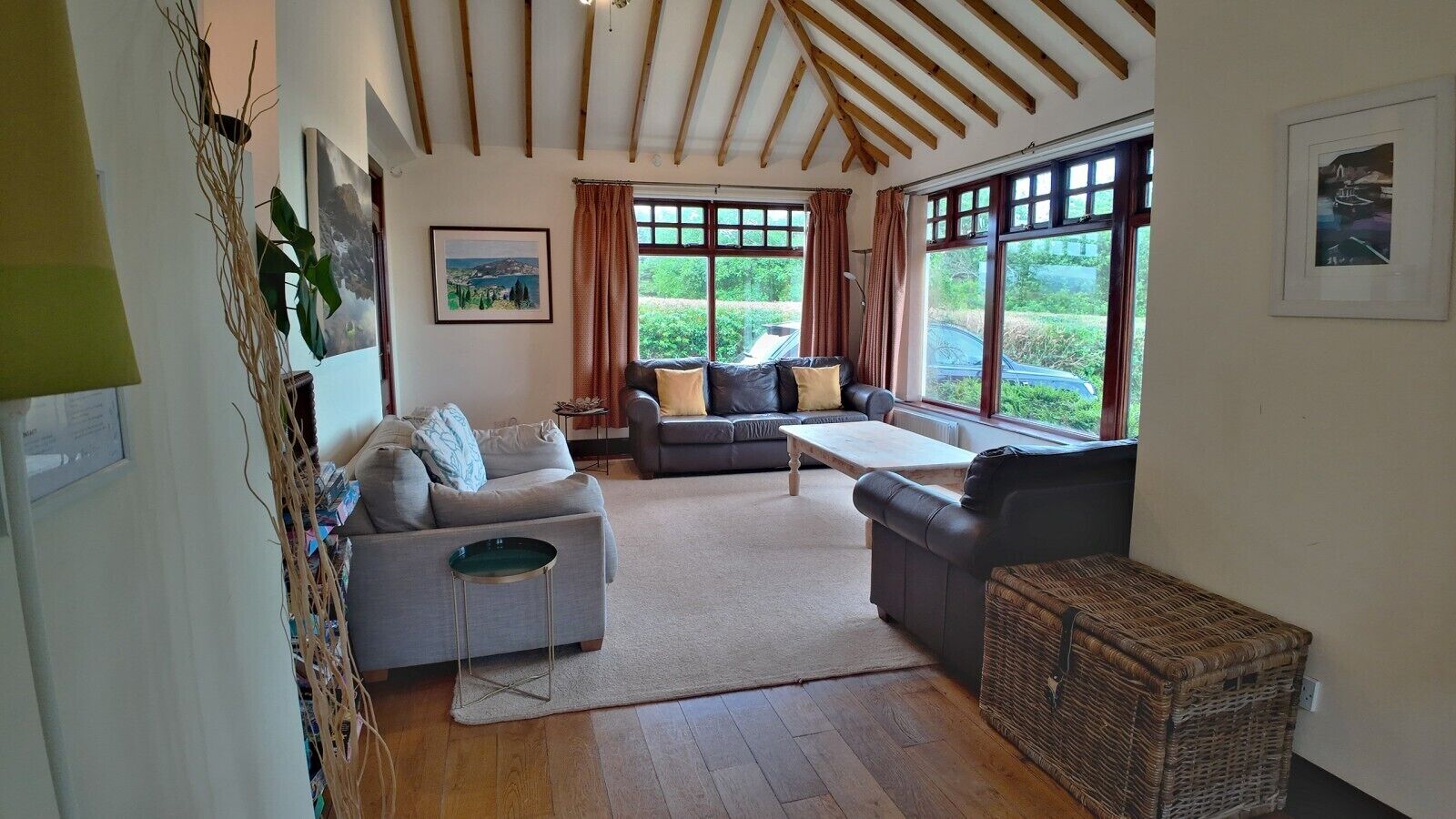 A spacious living room with a high ceiling, two sofas, a coffee table, and a large window providing a view of greenery.