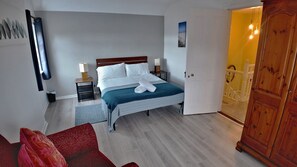 Ein Schlafzimmer mit Bett, Nachttischen, einem Kleiderschrank und einer Tür zu einem anderen Raum.