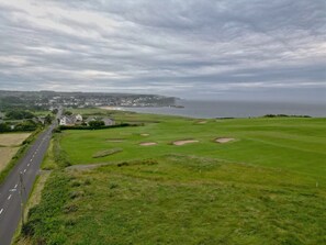 A coastal golf course with a road running alongside it, a distant town, and a view of the sea. - Thorn Cottage by Escape Ordinary (Ballycastle)