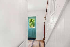 Un couloir avec une porte verte, des murs blancs et un escalier en bois.