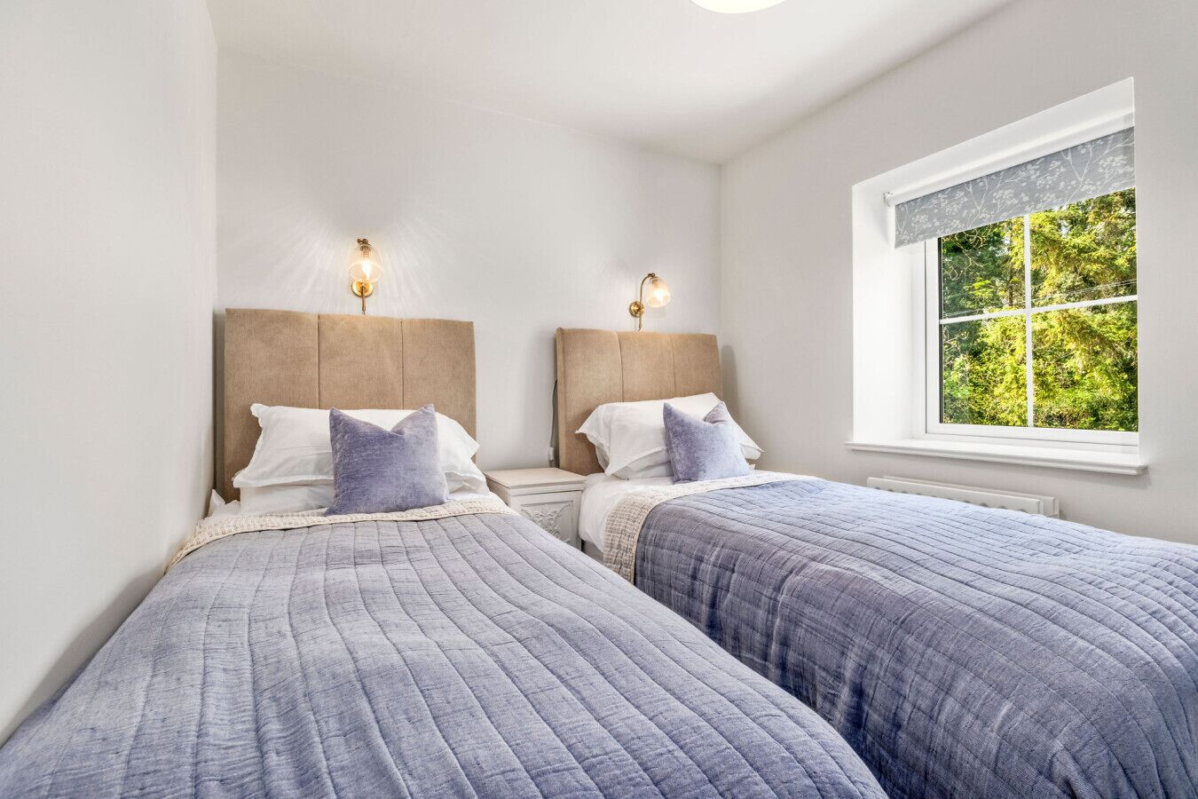 A bedroom with two beds, each with a headboard and bedside lamps.