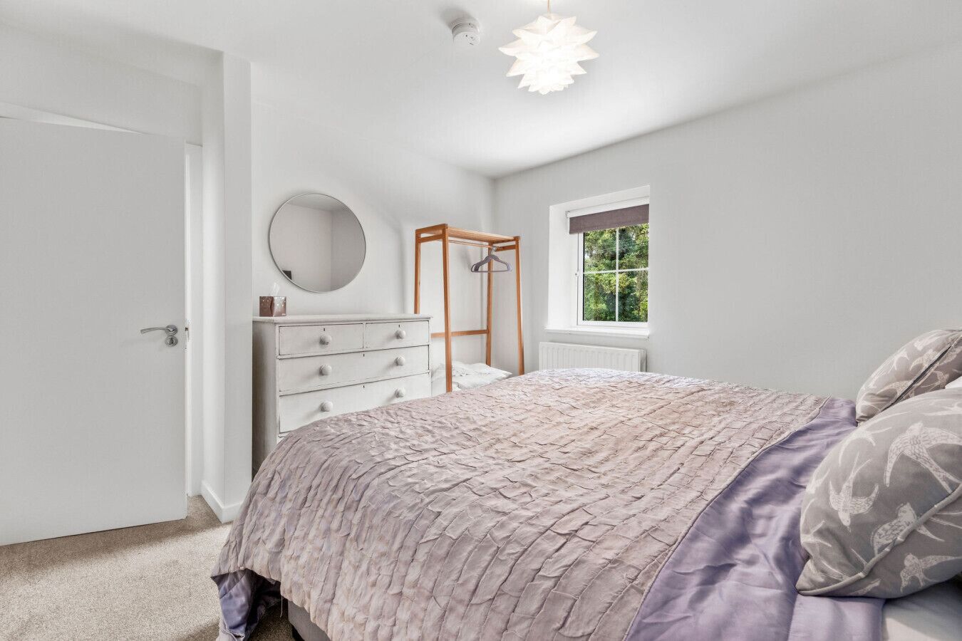 Ein Schlafzimmer mit Bett, Kommode, Spiegel und Fenster.