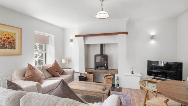 A modern living room with a sofa, a wooden coffee table, a TV, a fireplace, and a dining area. - Horseshoe Cottage by Escape Ordinary (Derrygonnelly)
