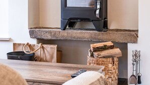 A wood-burning stove in a room with a stone hearth, a woven basket, and a remote control on a wooden table. - Horseshoe Cottage by Escape Ordinary (Derrygonnelly)