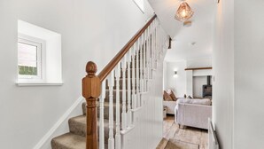 A staircase with wooden balusters and carpeted steps leading to a living area with a sofa and a fireplace. - Horseshoe Cottage by Escape Ordinary (Derrygonnelly)