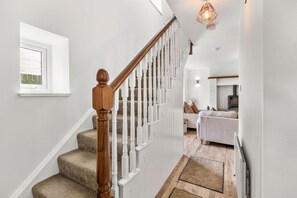 A staircase with wooden balusters and carpeted steps leading to a living area with a sofa and a fireplace. - Horseshoe Cottage by Escape Ordinary (Derrygonnelly)