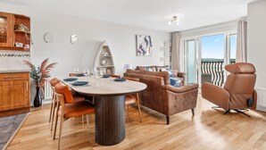 A modern living room with a dining area, a sofa, a chair, and a balcony with a view. - The Lookout · Dundrum Bay · Balcony with Bay Views (Dundrum)