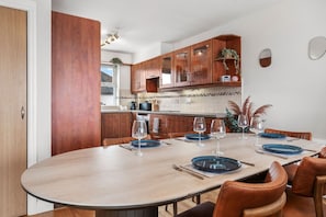 A modern kitchen with wooden cabinets, a dining table set for four, and a large window providing natural light. - The Lookout · Dundrum Bay · Balcony with Bay Views (Dundrum)