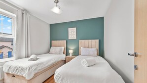 A bedroom with two beds, a window, a bedside table with a lamp, and a door. - The Lookout · Dundrum Bay · Balcony with Bay Views (Dundrum)