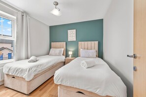Ein Schlafzimmer mit zwei Betten, einem Fenster, einem Nachttisch mit Lampe und einer Tür.