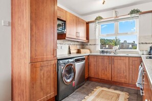 Eine moderne Küche mit Holzausstattung, einer integrierten Waschmaschine und einem Fenster mit Blick nach außen.