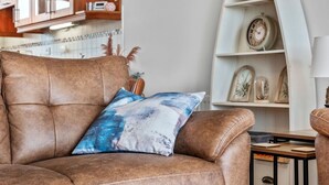 A brown leather sofa with a blue and white pillow, a wooden side table, and a white shelf with decorative items. - The Lookout · Dundrum Bay · Balcony with Bay Views (Dundrum)