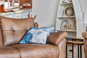 Ein braunes Ledersofa mit blau-weißem Kissen, ein Holznachttisch und ein weißes Regal mit Dekoration.