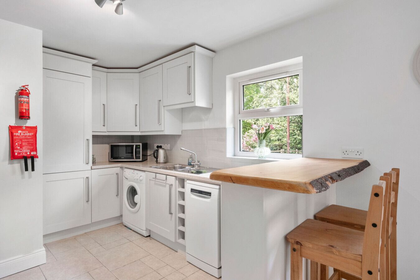 Cocina con armarios blancos, microondas, lavadora y encimera de madera.