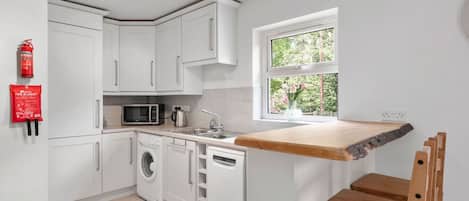 Cocina con armarios blancos, microondas, lavadora y encimera de madera.
