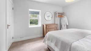 A bedroom with a bed, a dresser, a mirror, a window, and a hanging light fixture. - Orchard View Cottage | Escape Ordinary (Derrygonnelly)