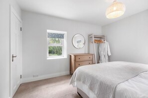 A bedroom with a bed, a dresser, a mirror, a window, and a hanging light fixture. - Orchard View Cottage | Escape Ordinary (Derrygonnelly)
