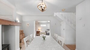 A dining area with a long table, white chairs, a chandelier, and a staircase. - Orchard View Cottage | Escape Ordinary (Derrygonnelly)