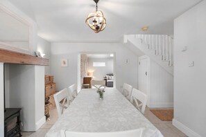 A dining area with a long table, white chairs, a chandelier, and a staircase. - Orchard View Cottage | Escape Ordinary (Derrygonnelly)
